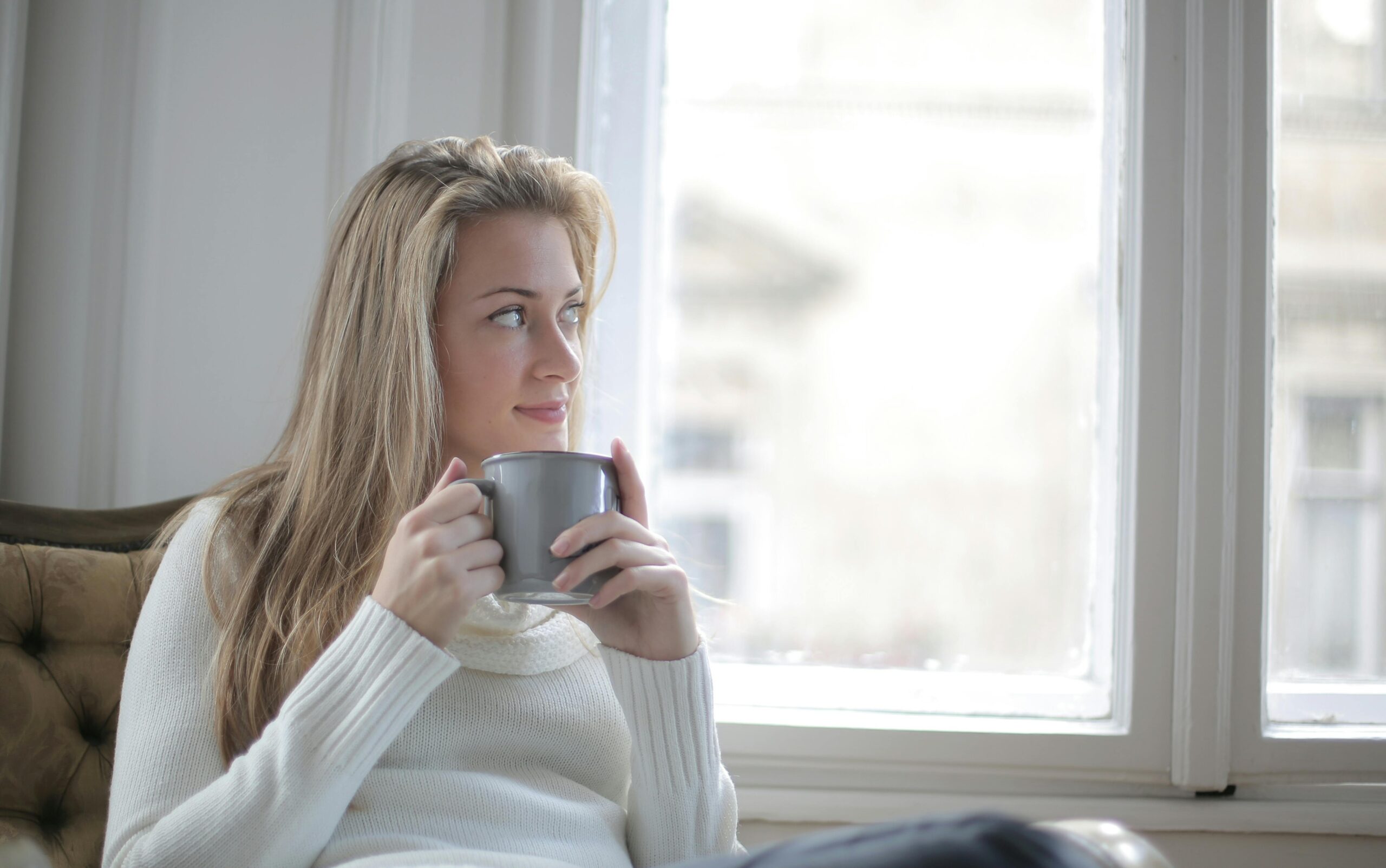 Person sitting by a window holding a warm mug, looking calm and reflective, representing the psychology of happiness and everyday moments of wellbeing.