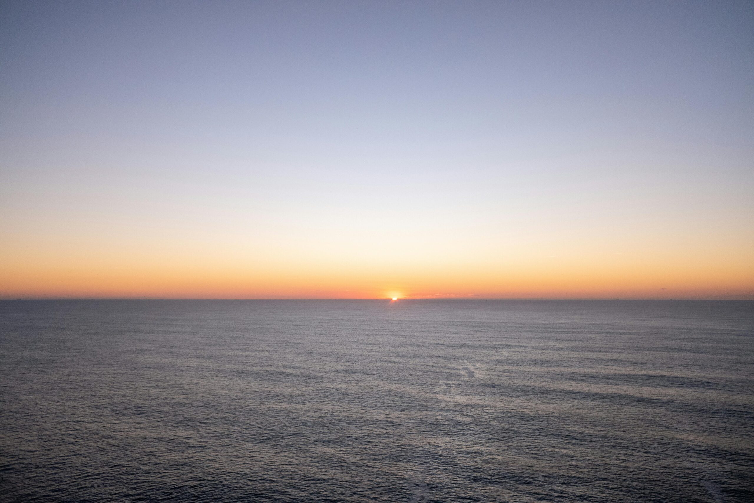 A calm ocean horizon at sunrise with soft warm light reflecting across still water.